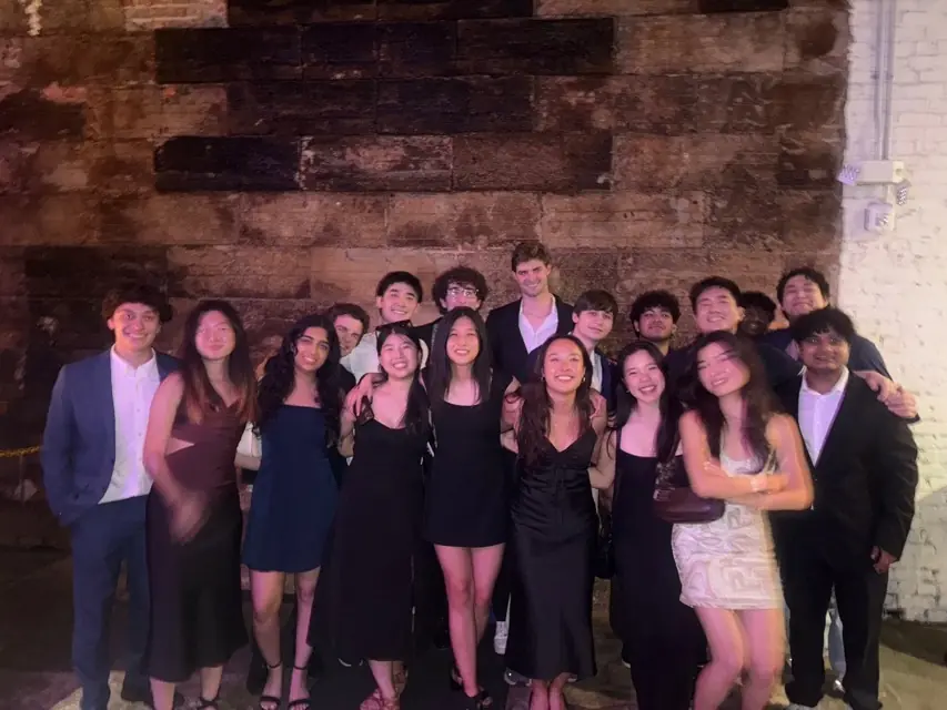 A large group in dresses and suits lined up against a brick wall at night